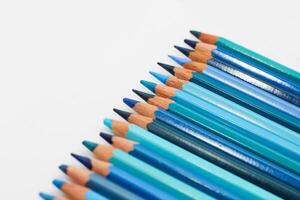 Multi-colored pencils lie on a white table, the blue range of colors photo