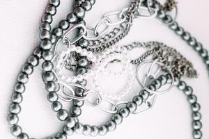 A necklace of gray beads with chain decorations on a white aesthetic background. photo