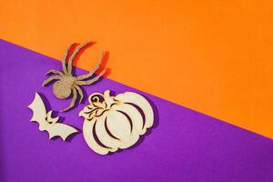 Wooden toy spider, pumpkin, bat on orange and purple background Halloween concept photo