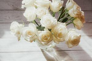 White roses stand in a vase on white wooden boards. photo