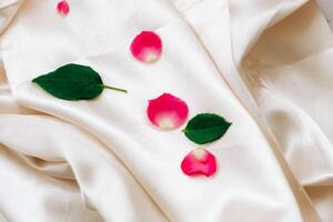 Petals of pink roses on a white silk background with space for text. photo