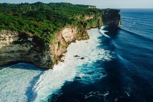 Rocky cliff coastline and ocean with waves near Uluwatu temple in Bali photo