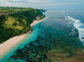 Tropical beach with cliffs, ocean and sunshine in Bali island. Aerial view of vacation beach photo