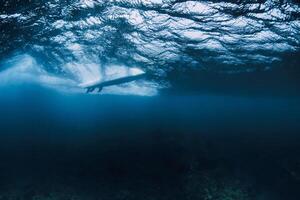 Wave underwater and surfer on surfboard in ocean. Underwater crashing wave and surfboard during surfing photo