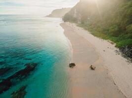 Beach with ocean, green cliffs and sunshine in Bali. Aerial view of tropical vacation coastline photo