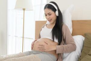 Happy pregnant woman with headphones listening to mozart music and lying on bed, pregnancy concept photo