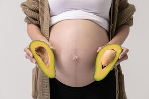 Portrait of Beautiful pregnant woman holding avocado over white background studio, health and maternity concept photo