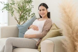 Happy pregnant woman with headphones listening to mozart music and lying on sofa, pregnancy concept photo