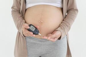 Pregnant woman checking blood sugar level by using Digital Glucose meter, health care, medicine, diabetes, glycemia concept photo