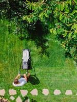 Caucasian gardener mowing backyard garden grass using Cordless electric grass mower. Aerial View. photo