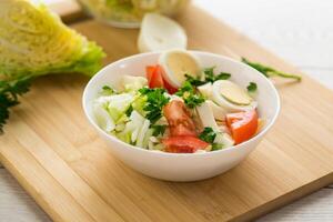 fresh vegetable salad, cabbage, tomatoes in a bowl on a wooden table photo