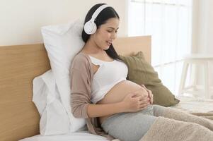 Happy pregnant woman with headphones listening to mozart music and lying on bed, pregnancy concept photo