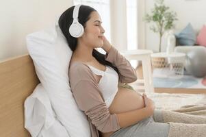 Happy pregnant woman with headphones listening to mozart music and lying on bed, pregnancy concept photo
