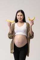 retrato de hermosa embarazada mujer participación plátano terminado blanco antecedentes estudio, salud y maternidad concepto foto