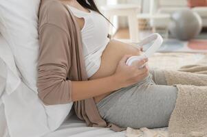 Happy pregnant woman with headphones listening to mozart music and lying on bed, pregnancy concept photo