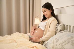 Beautiful pregnant woman applying moisturizing, stretch mark cream on belly, fertility infertility treatment, IVF, future maternity concept photo