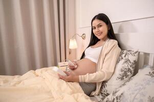 Beautiful pregnant woman holding pocket fetal doppler to listen baby's heartbeat on belly, fertility infertility treatment, IVF, future maternity concept photo