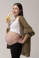 retrato de hermosa embarazada mujer participación plátano terminado blanco antecedentes estudio, salud y maternidad concepto foto