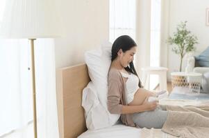 Happy pregnant woman with headphones listening to mozart music and lying on bed, pregnancy concept photo