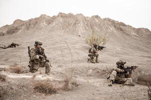 Soldiers in camouflage uniforms aiming with their rifles ready to fire during military operation in the desert , soldiers training in a military operation photo