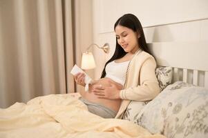 hermosa embarazada mujer aplicando hidratante, tramo marca crema en barriga, Fertilidad esterilidad tratamiento, FIV, futuro maternidad concepto foto