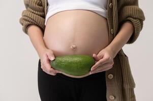 Portrait of Beautiful pregnant woman holding avocado over white background studio, health and maternity concept photo