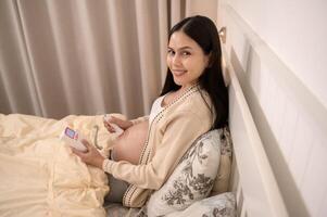Beautiful pregnant woman holding pocket fetal doppler to listen baby's heartbeat on belly, fertility infertility treatment, IVF, future maternity concept photo