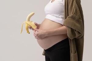 retrato de hermosa embarazada mujer participación plátano terminado blanco antecedentes estudio, salud y maternidad concepto foto