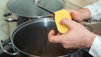 pellen een aardappel over- een pot, een persoon is pellen een aardappel over- een pot in een keuken, voorbereidingen treffen een maaltijd. de focus is Aan de handen en de aardappel, markeren de routine- van huis Koken. video