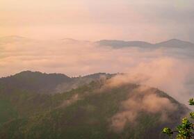 The stunning view from a tourist's standpoint as they go down a hill on a foggy trail with a hill and a background of a golden sky in Forest Park, Thailand. Rainforest. Bird's eye view. Aerial view. photo