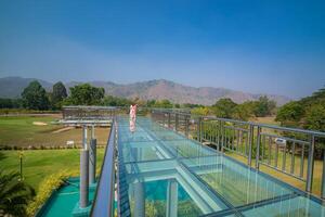 A sky walk at a scene with a mountain, and bridge with a glass floor and stainless steel railing.View from the Vajralongkorn Dam, Kanchanaburi, Thailand. photo