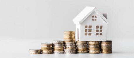 White wooden house models stands on a stacks of coins, solid white background with copy space, finance, mortgage, investment, real estate concept photo