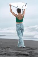 Rear view of female surfer walking on beach with white surfboard on head on background ocean waves photo