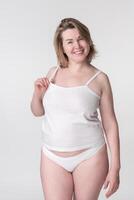 Cheerful full figured woman wearing white cotton camisole and panties, posing on white background photo