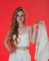 Stylish woman wearing white sculpting corset top and holding jacket in hand, poses on red background photo