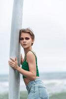 Portrait of sensual woman holding surfboard with both hands, presses against it and looking away photo