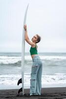 Side view woman surfer arms raised, holding surfboard vertically. Full length female on sandy beach photo