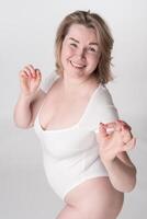 Happiness radiates from woman dressed bodysuit as she confidently shows OK sign. Body positive model photo