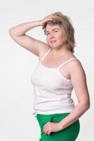 Mid adult woman with plump figure poses with one hand raised to head, standing on white background photo