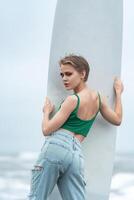 Rear view of sensuality woman surfer holding surfboard vertically, looking over shoulder at camera photo