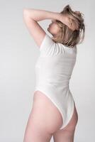 Three quarter view from rear of plump female in bodysuit posing with hands raised behind head photo