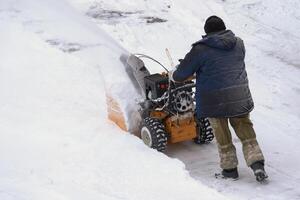 A man is using a snow blower to remove snow after a winter storm. He is assisted by a thrower on a winter road. photo