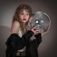 Confident young woman holding and presses disco ball to herself, looking away during party in club photo