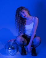 Woman with disco ball posing in squatting while partying in nightclub. She exudes sensuality photo