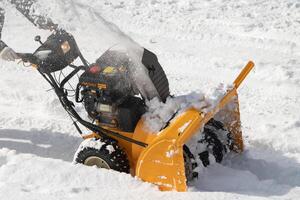 Worker with motor snowblower clearing snow from road after winter storm, assisted by snow thrower. Mechanized snow removal from roadway photo