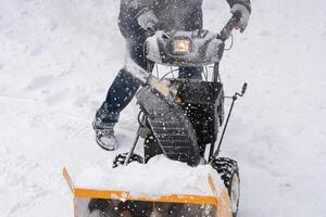 An unidentified individual is operating a snow blower to clear snow from a winter road, with the aid of a snow blower, following a winter storm. photo