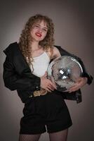 Smiling young adult woman holding disco ball and looking at camera. Cheerful young adult pin up girl photo