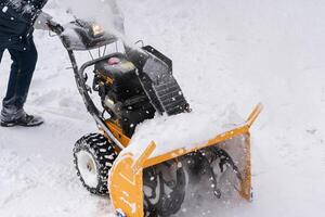 A male worker is using a snow blower to clear snow from a winter road after a snowstorm photo