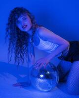 Sensuality woman with long curly hair holds mirror disco ball and looking at camera, posing kneeling photo