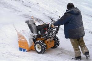 A man is using a snowblower to clear snow after a winter storm. He is being assisted by a snow thrower on a winter road photo